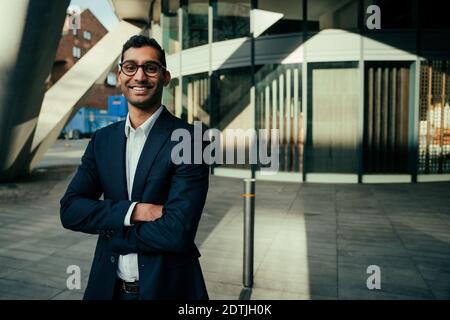 Mixed race businessman smiling standing with crossed arms in front of office Stock Photo