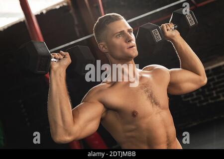 Young handsome bodybuilder doing shoulder press in the gym Stock Photo