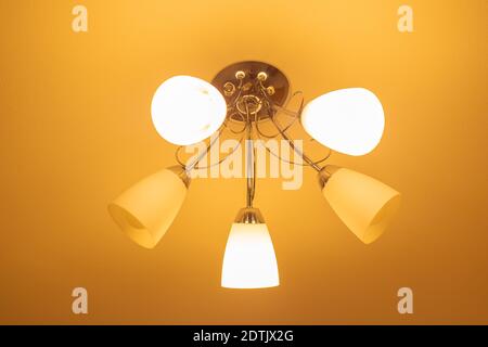chandelier of five arms on the ceiling, shining with yellow light. Lighting and room decor. Stock Photo