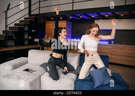 Beautiful best girlfriends have video games competition at home while having rest time. Enjoying vacation time to spend leisure with friends. Stock Photo