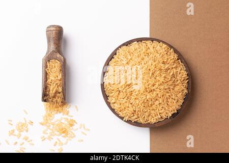 Wooden plate and spoon with brown rice, on  white and brown background. Flat lay composition. Stock Photo
