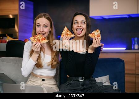 Two female best friends having fun at home, with tasty pizza at home party. Staying home and use food delivery during quarantine. Stock Photo