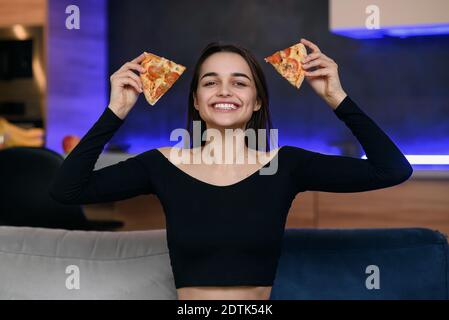 Excited happy young woman in kitchen playing with pizza slices, smiling and feeling happiness. Carefree girl very playful. Pizza delivery online. Stock Photo