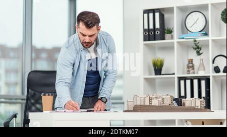 Handsome senior architect working on a construction project and examines the model on which he works. Stock Photo