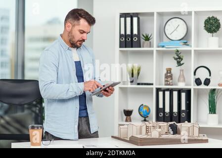 Handsome senior architect working on a construction project using innovation technologies. Caucasian man with tablet pc at office. Stock Photo