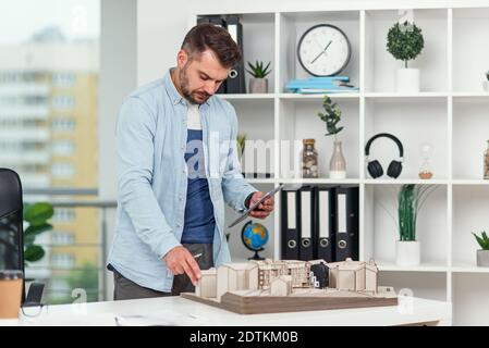 Handsome senior architect working on a construction project and examines the model on which he works. Stock Photo