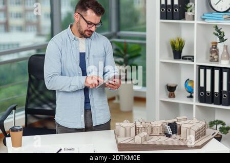 An experienced male architect in office inspects the project of a residential complex and makes calculations using a tablet PC. Stock Photo