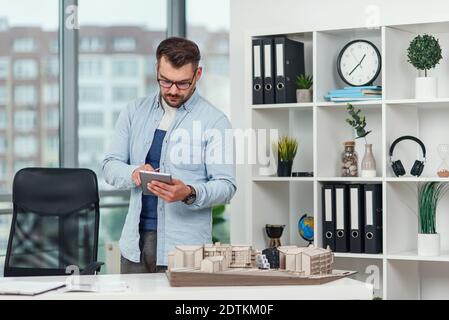 Handsome senior architect working on a construction project using innovation technologies. Caucasian man with tablet pc at office. Stock Photo
