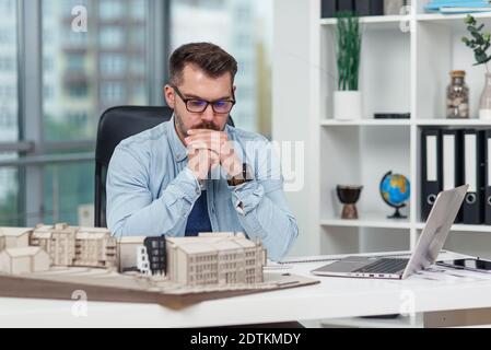 Handsome senior architect working on a construction project, he examines the model on which he works Stock Photo