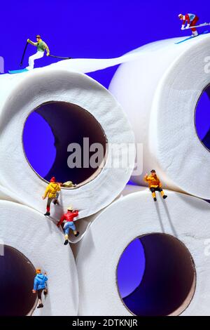 Conceptual image of miniature figure people skiing on toilet roll tissue whilst climbers scale the outside of the tubes