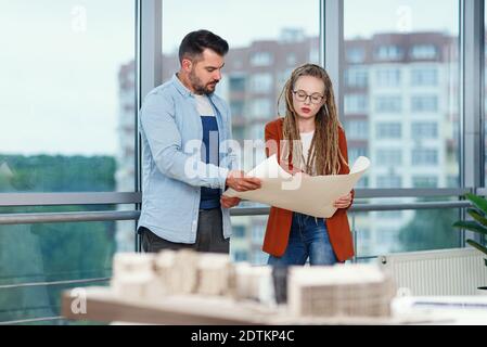 Confident bearded male designer and his female colleague with dreadlocks analysing printed on paper project. Stock Photo