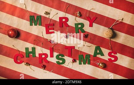 Flat-lay of Merry Christmas words made up with decorative red and green letters over vintage craft striped wrapping paper, top view. Christmas holiday greeting banner concept Stock Photo
