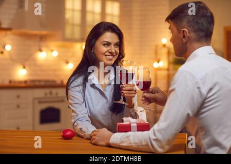 Young loving couple sitting together in kitchen, holding hands, drinking wine during Valentines day Stock Photo