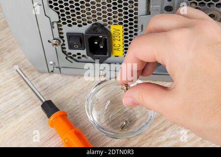 Woman hand removed the screw holding the power supply unit in the pc case and puts it in the glass bowl on a desk. Personal computer PSU replasing. Stock Photo