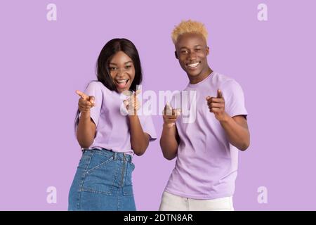 Portrait of cheerful black couple pointing at you over lilac studio background Stock Photo