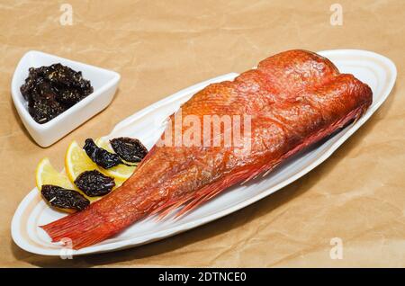 Hot smoked sea bass with lemon and dried spicy plums, close-up on a background of crumpled paper. Delicious seafood for proper nutrition Stock Photo