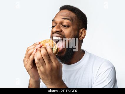 African Man Eating Burger Greedily Enjoying Fastfood Over White Background Stock Photo