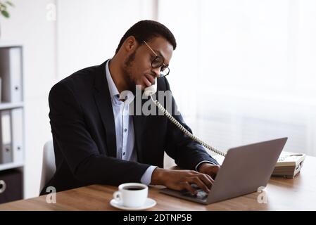 Busy black manager talking on phone and using laptop Stock Photo