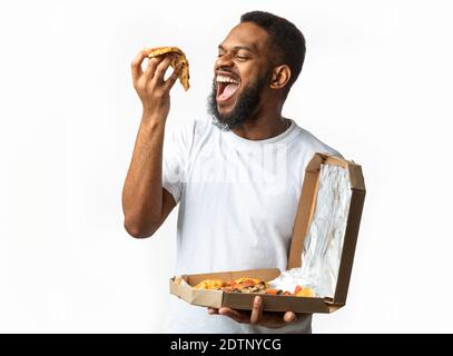 Hungry Black Guy Eating Pizza Slice Standing Over White Background Stock Photo