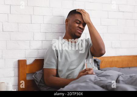 Black Guy Suffering From Headache Sitting In Bed At Home Stock Photo