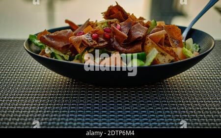 Fattoush (Lebanese salad) close up  image in a black plate . It is made with vegetables and crispy toasted flatbread, which soaks up the dressing Stock Photo