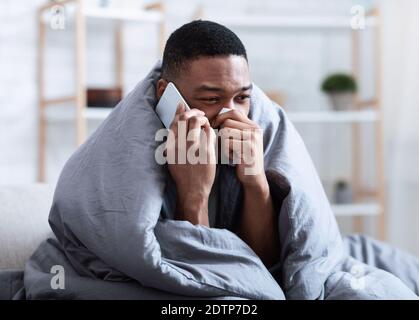 Ill Black Man Calling Doctor Having Runny Nose Sitting Indoors Stock