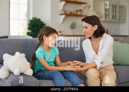 Sad girl having therapy session with child psychologist sitting on sofa in privacy of her own home Stock Photo