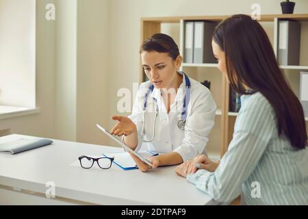 Woman doctor therapist communicating with patient and showing her research results during visit in medical clinic Stock Photo