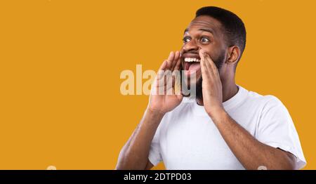 African Man Shouting Holding Hands Near Mouth Over Yellow Background Stock Photo