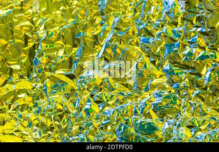 Metal chrome wrinkle texture with yellow tint and glance effect and crumpled structure with holographic iridescent effect with lime illuminating brigh Stock Photo