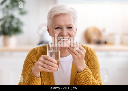 Happy senior lady holding glass of water and pill