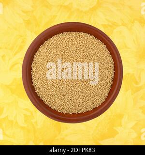 Top view of amaranth seeds in a small bowl on a yellow floral background. Stock Photo