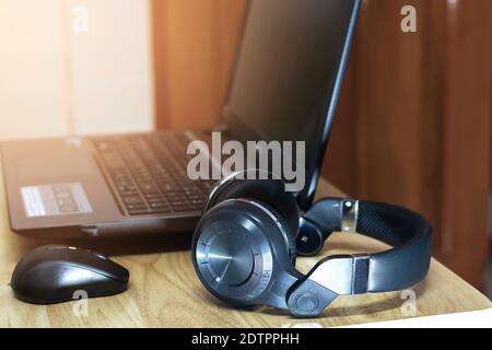 Closeup a headphone on the wooden table with a wireless mouse and computer notebook. Stock Photo