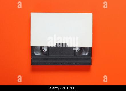 The videotape in a paper case on orange background. Pop culture attributes, minimalism. Top view Stock Photo