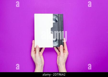 Female hands holding video cassette in cover on  purple background. Top view Stock Photo