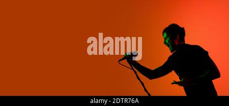 Flyer. Silhouette of young male guitarist isolated on orange gradient studio background in neon. Beautiful shadow in action, performing. Concept of human emotions, expression, ad, music, art. Stock Photo