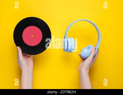 Women's hands hold over-ear headphones and vinyl record on yellow background. Pop culture, retro style, 80s. Minimalism. Top view. Flat lay Stock Photo