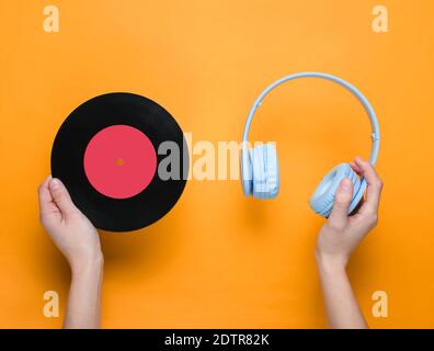 Women's hands hold over-ear headphones and vinyl record on orange background. Pop culture, retro style, 80s. Minimalism. Top view. Flat lay Stock Photo
