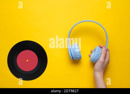 Women's hands hold over-ear headphones and vinyl record on yellow background. Pop culture, retro style, 80s. Minimalism. Top view. Flat lay Stock Photo
