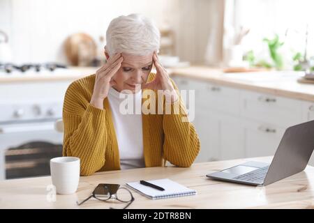 Tired mature woman freelancer working from home, using laptop Stock Photo