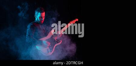Flyer. Silhouette of young male guitarist isolated on blue-pink gradient studio background in neon. Beautiful shadow in action, performing. Concept of human emotions, expression, ad, music, art. Stock Photo