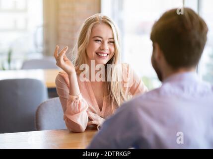 Romantic young lady having friendly chat with her boyfriend at cafe, spending time with her lover, flirting and smiling Stock Photo