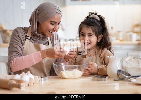 Happy islamic mom and her cute daughter preparing dough in kitchen together Stock Photo