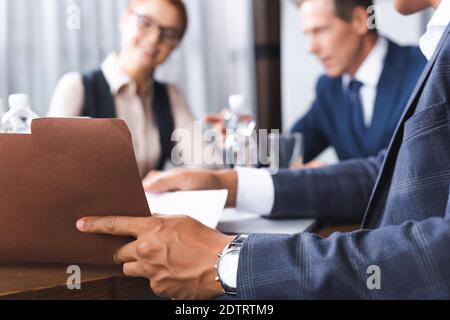 Close up view of african american businessman opening paper folder at workplace with blurred businesspeople on background Stock Photo