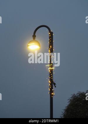 A vertical shot of a street lamp with Christmas lights wrapped around the post Stock Photo