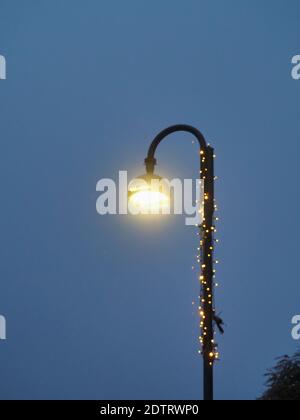 A vertical shot of a street lamp with Christmas lights wrapped on the post Stock Photo