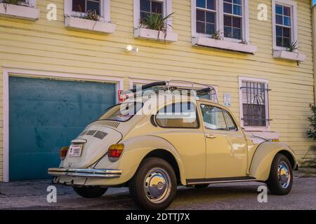 A classic, yellow Volkswagen Beetle car next to a yellow building. Stock Photo