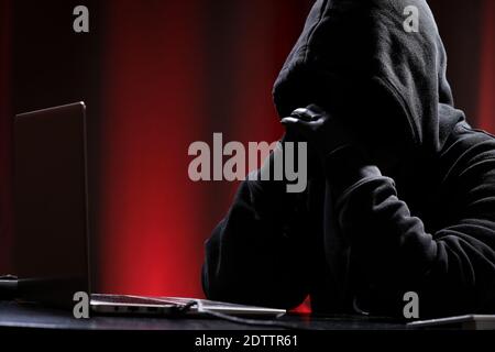 International hacker in black pullover and black mask trying to hack government on a black and red background. Cyber crime . Cyber security. Stock Photo