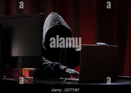 International hacker in black pullover and black mask trying to hack government on a black and red background. Cyber crime . Cyber security. Stock Photo