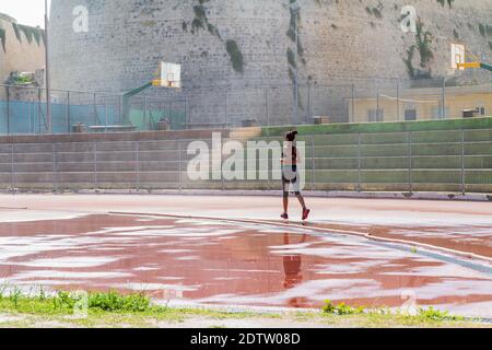 Woman runner jogging on wet red run lane at stadium. Stock Photo